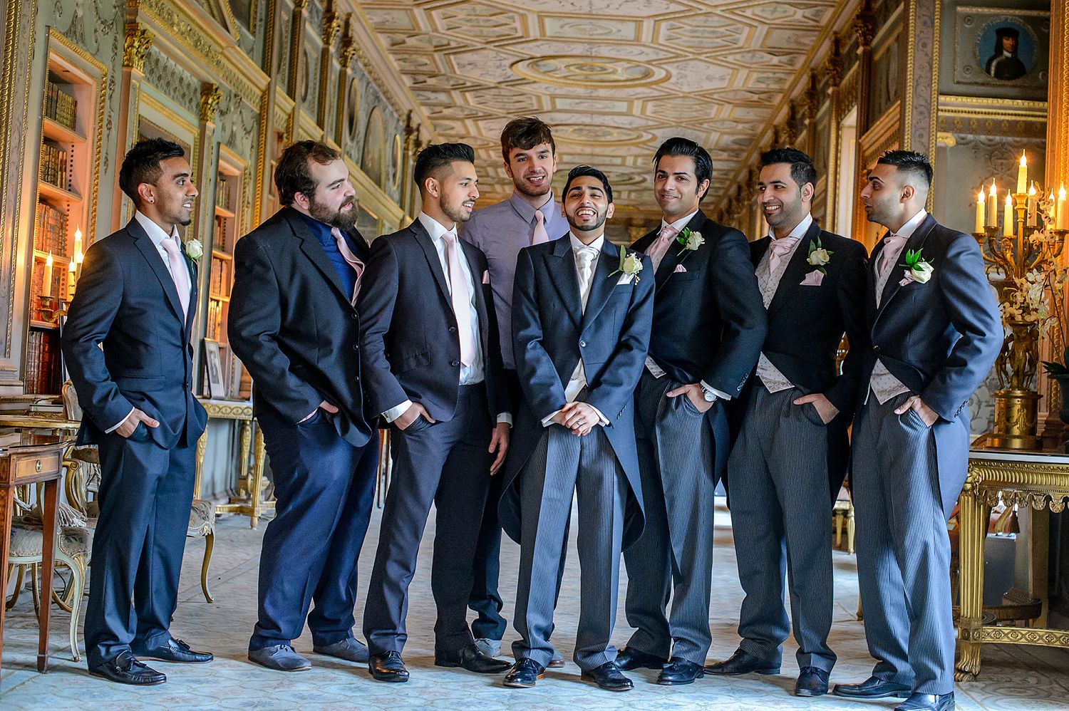 Groomsmen in navy suits stand together in an ornate hallway with gilded walls and decorative ceiling.