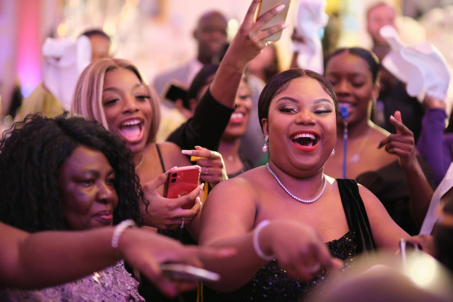 Excited party guests dance and celebrate at a lively event with colorful lighting and joyful expressions.