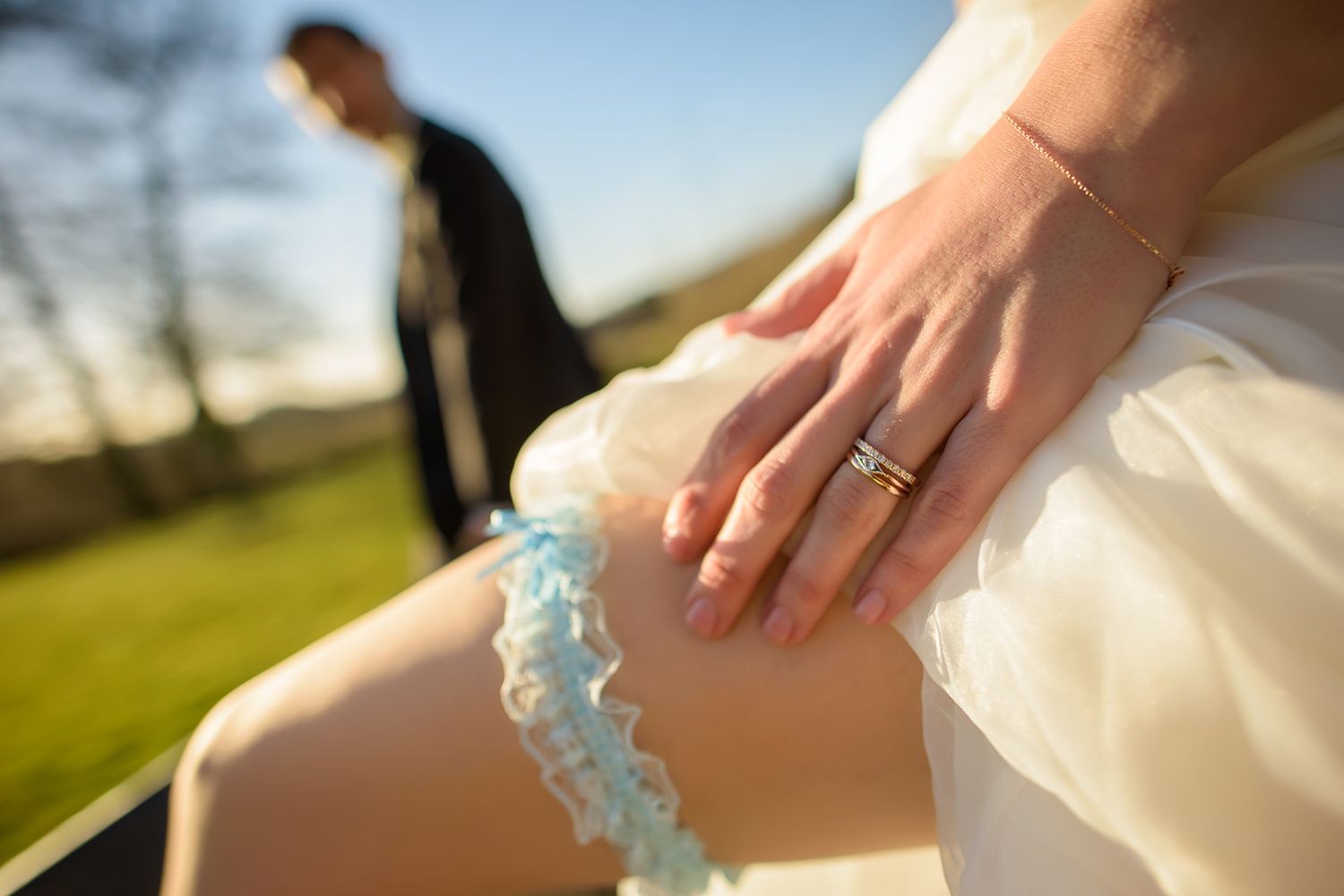 Detail shots of wedding dress and blue garter being adjusted outdoors.