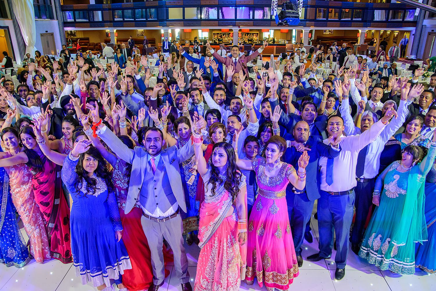 Large group celebration with guests in colorful traditional attire dancing together.