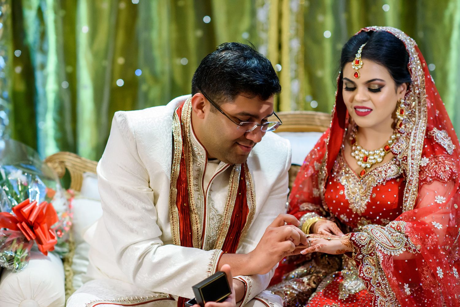Traditional Indian wedding ceremony with couple in red and white attire against green backdrop.