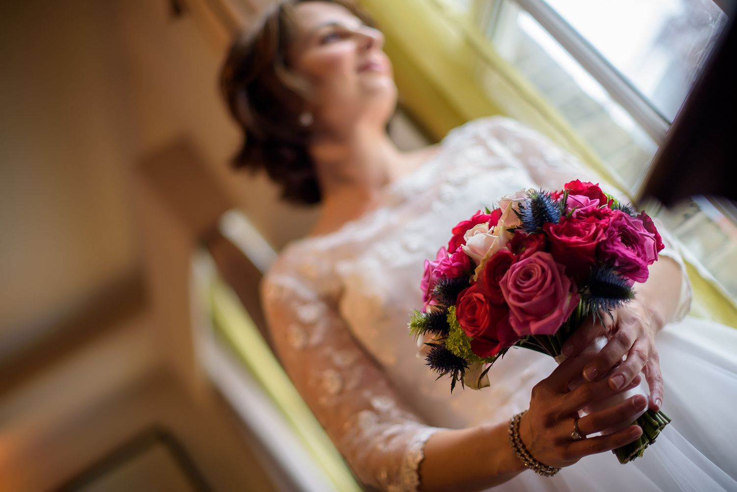 Vibrant pink and red bridal bouquet held against natural window light.