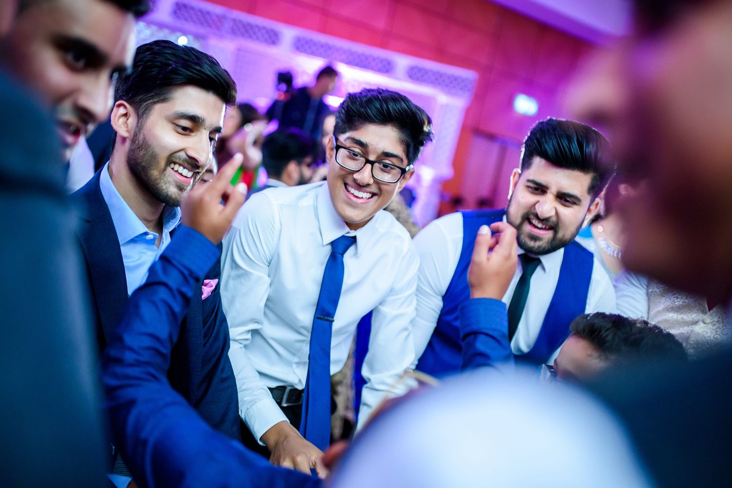 Guests at an Indian wedding reception share joyful moments under purple ambient lighting.