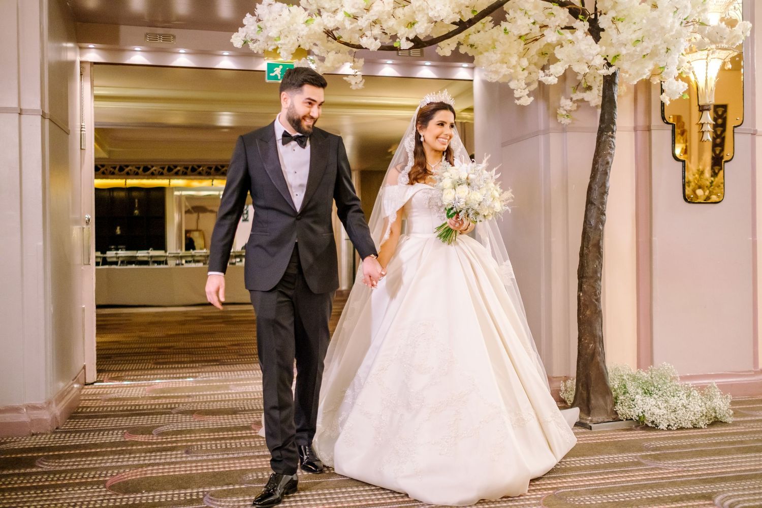 An elegant wedding couple walking through a luxurious venue with crystal chandeliers and marble floors.