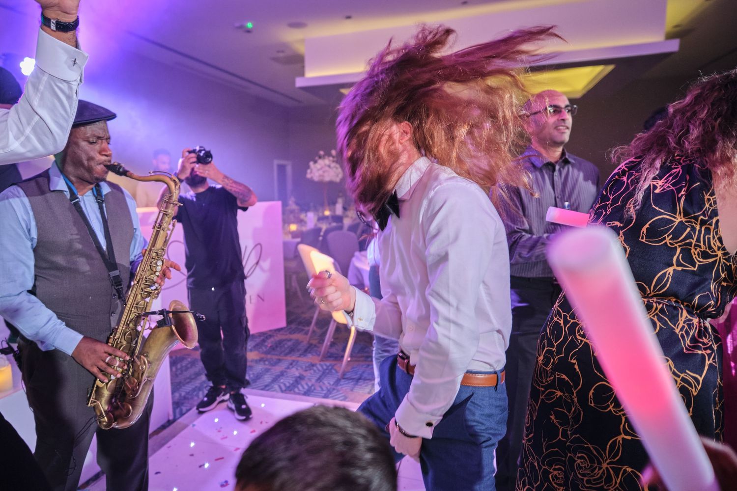 Live band performs at a party with saxophone player and dancers in purple-lit venue.