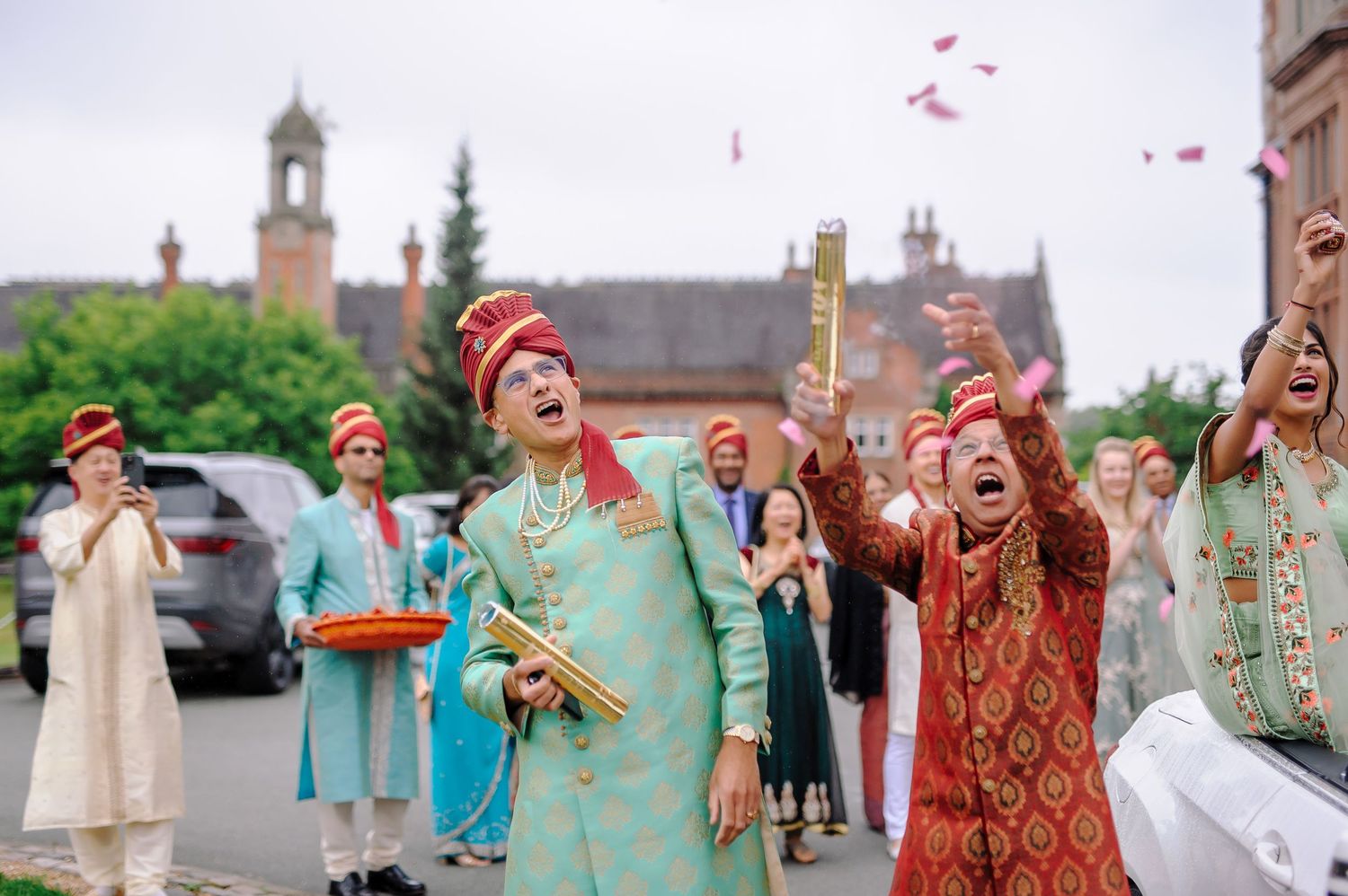 Guests in traditional Indian outfits celebrate by throwing rose petals during outdoor wedding festivities.