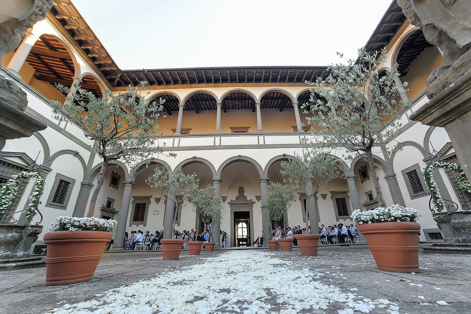 Wedding reception setup in a historic courtyard with arched columns and terracotta planters.