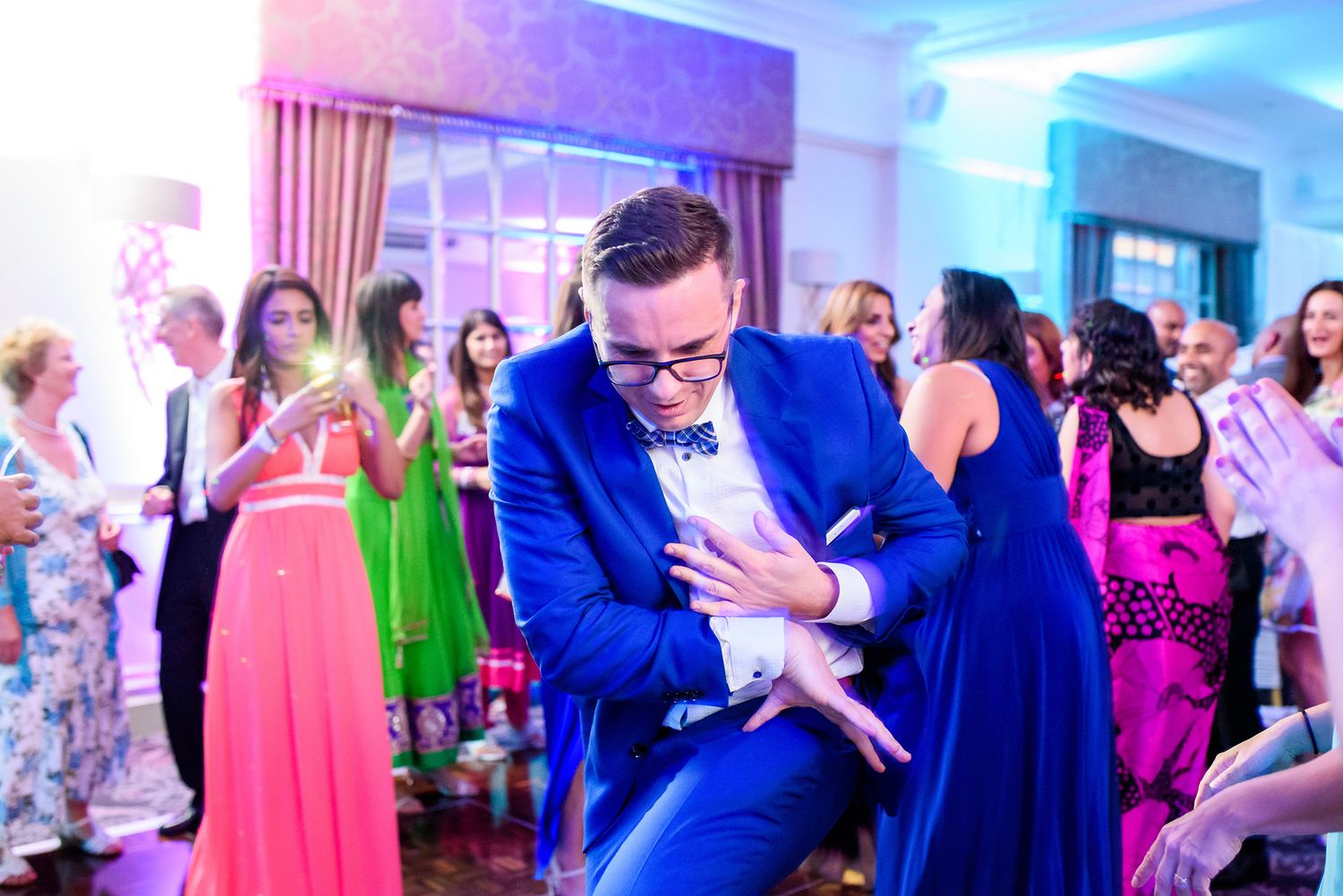 Wedding guests dancing in formal attire under elegant lighting at an evening reception.