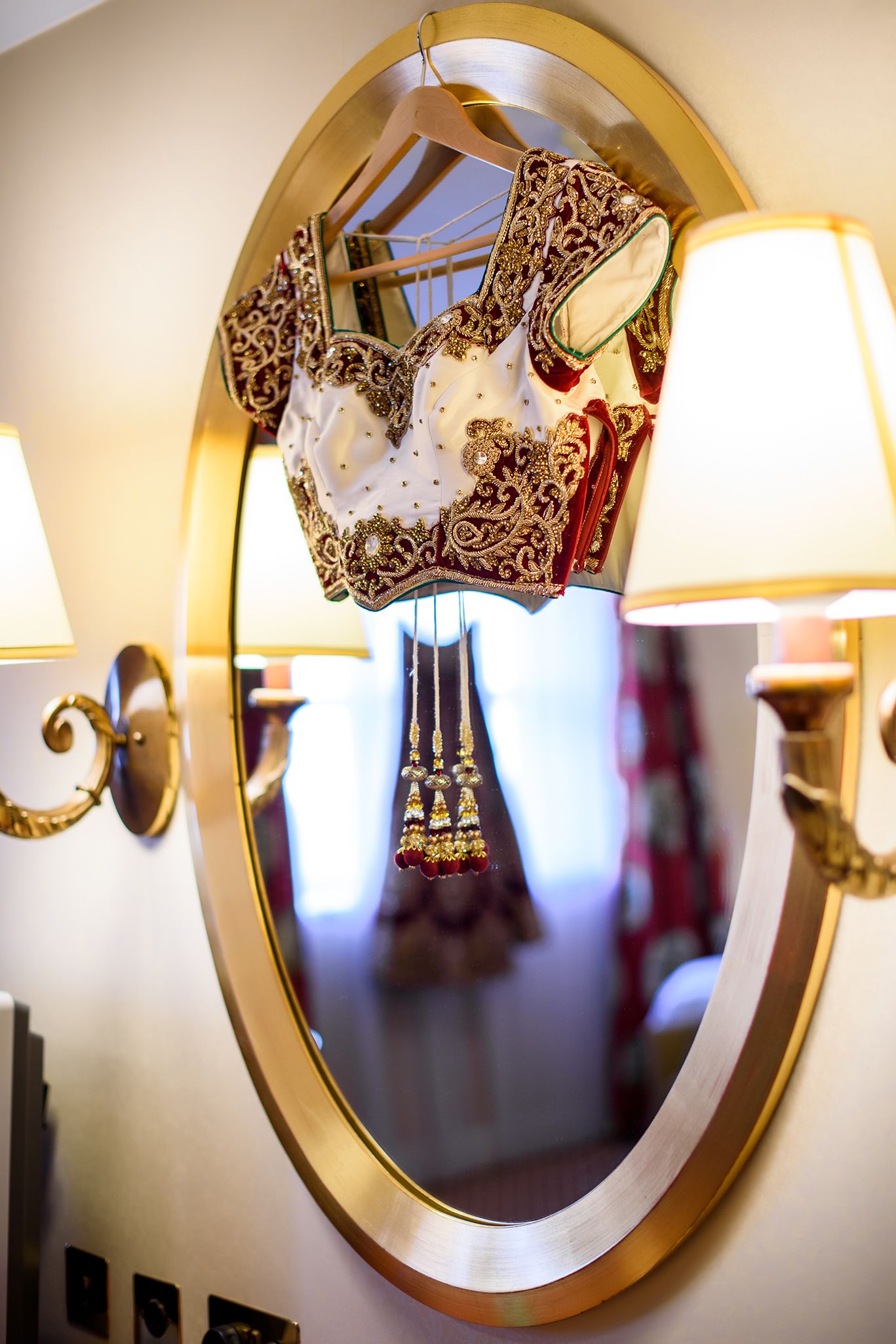 Wedding dress details displayed in golden round mirrors with elegant wall lighting.