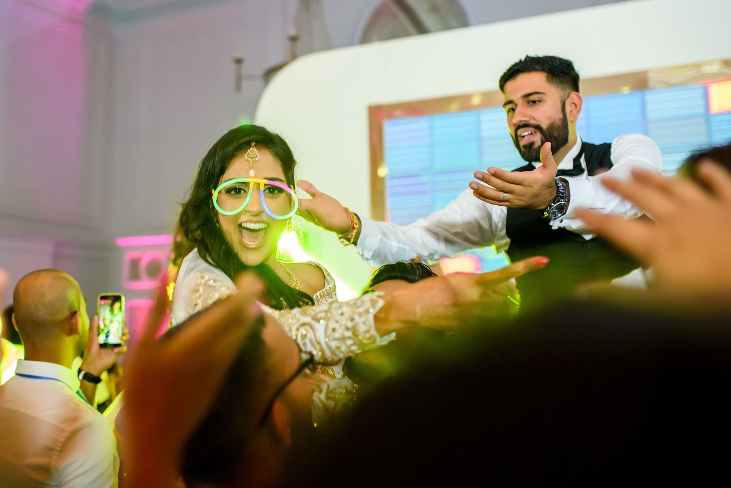 Guests celebrate with raised arms and expressions of joy at a wedding reception.