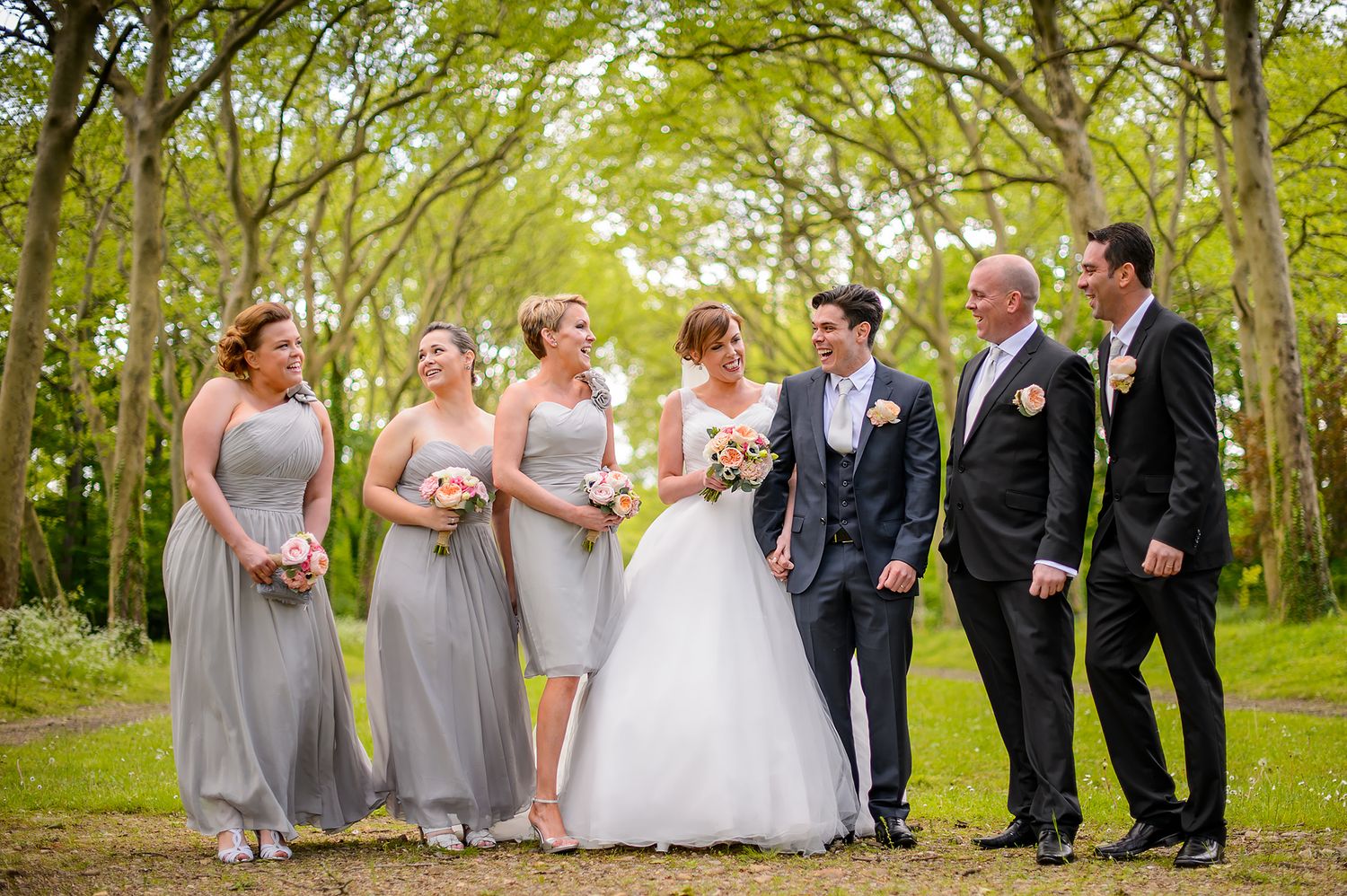 Wedding party poses together under trees in a scenic outdoor setting.
