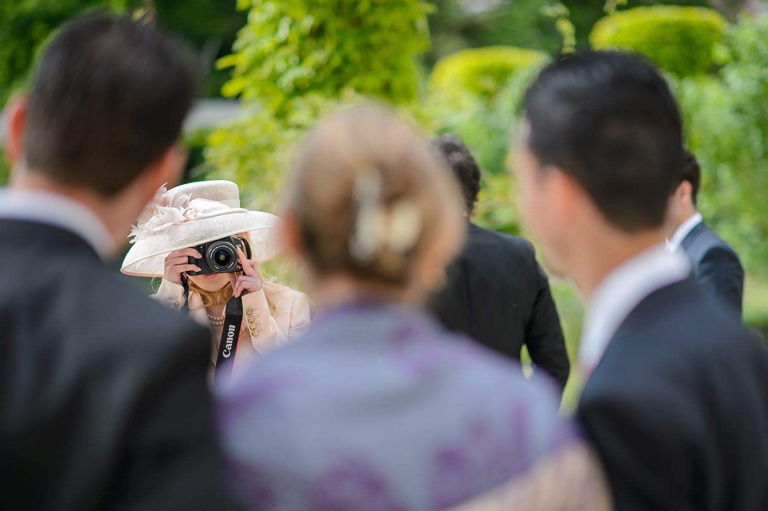 Wedding guests gathered outdoors on a sunny day with lush green foliage in the background.