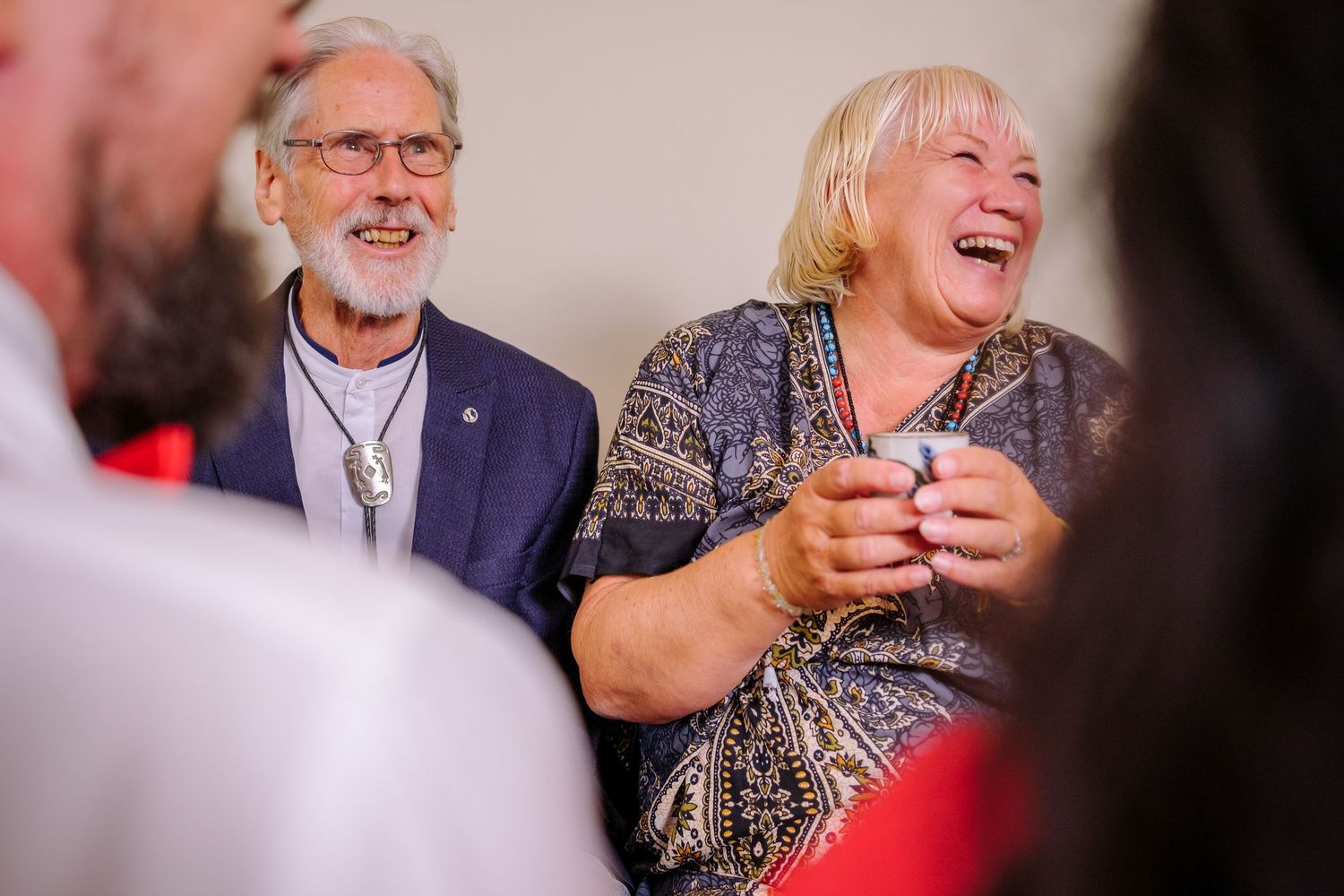 Guests at a celebration share laughter and smiles while seated at an indoor event.