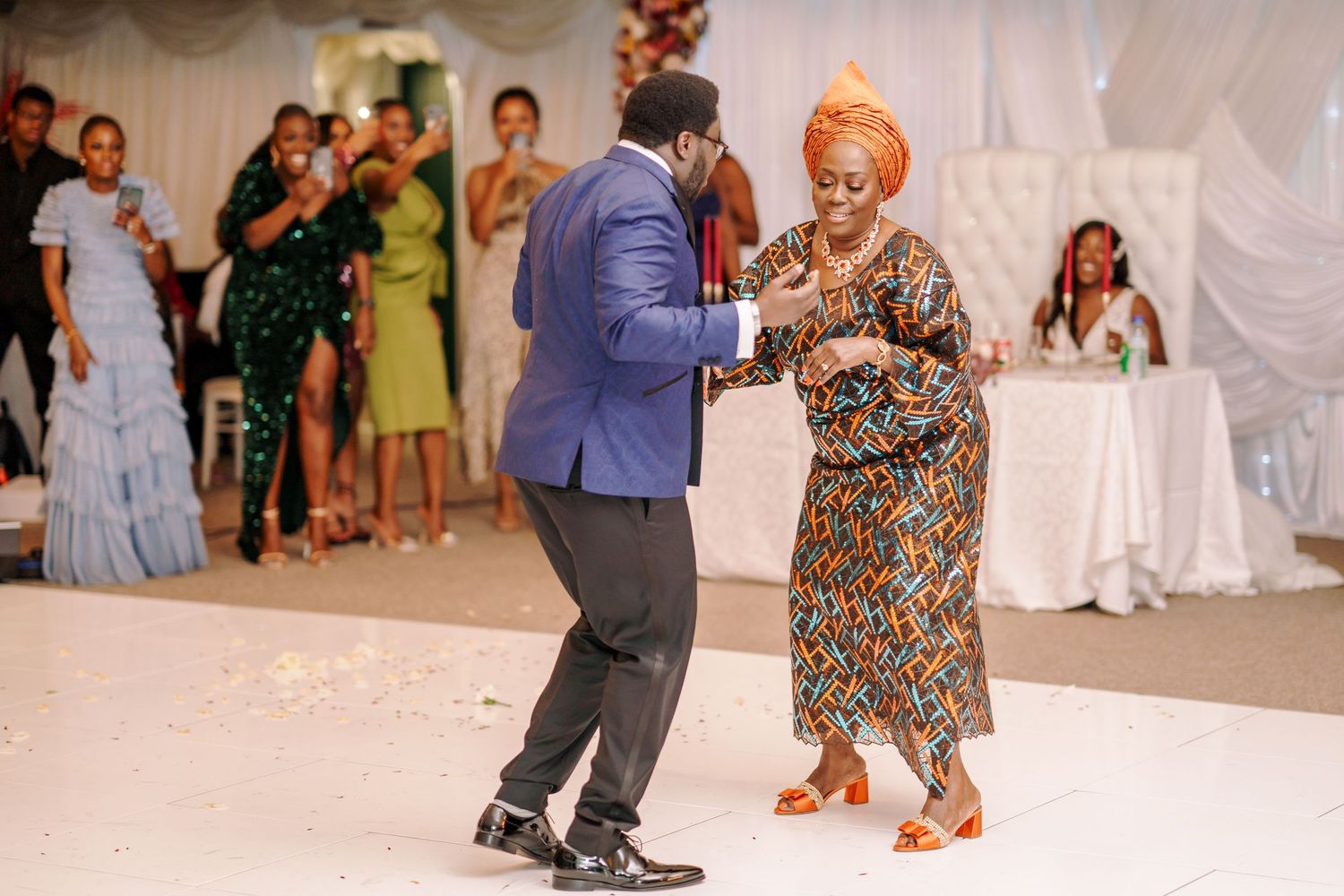 Dancers perform energetic moves on a white dance floor during a festive celebration with decorative elements.