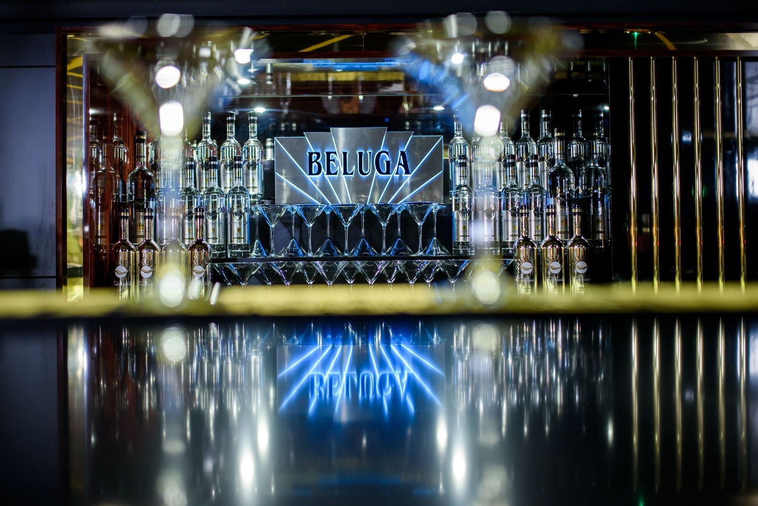 Row of illuminated glass bottles displayed behind a modern bar counter with blue accent lighting.
