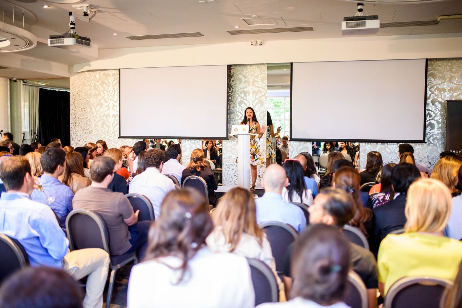 Large crowd of attendees gathered in a bright conference room for a business presentation.