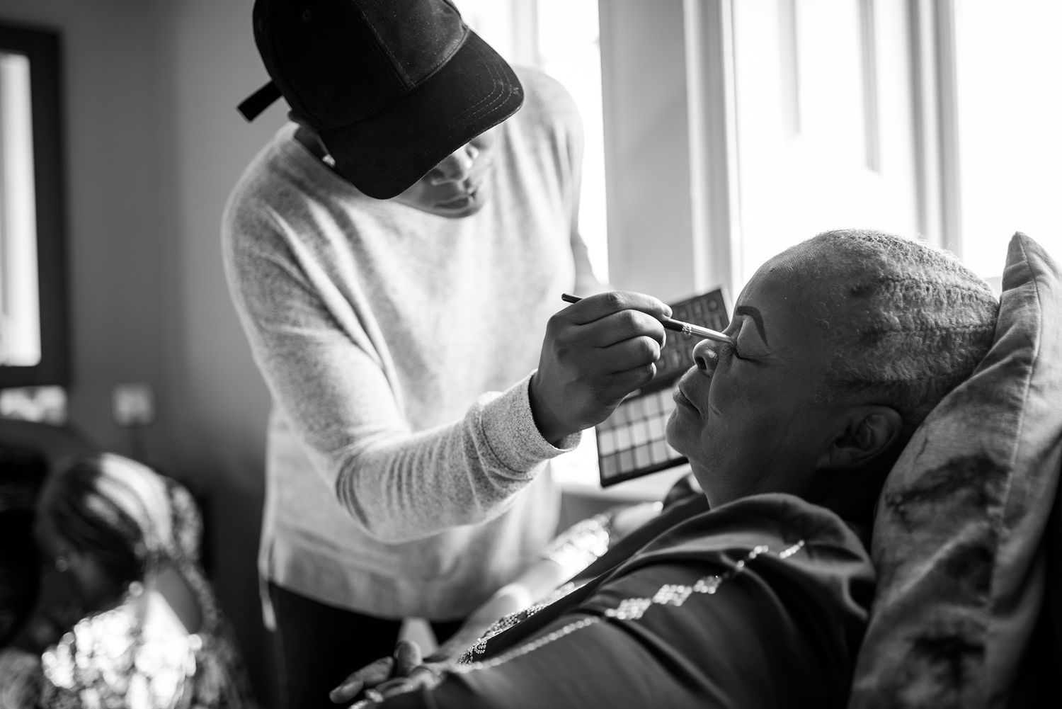 Wedding party members get ready in a bright sunlit room wearing formal attire.