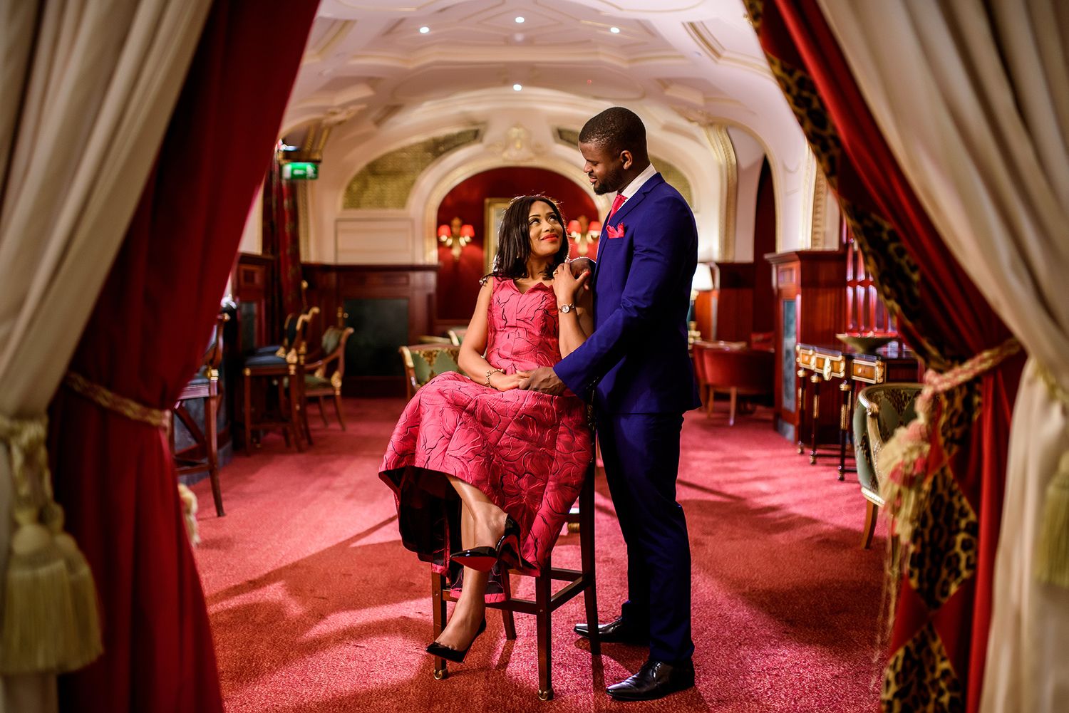 An intimate scene unfolds in a luxurious room with red carpeting and dramatic lighting.