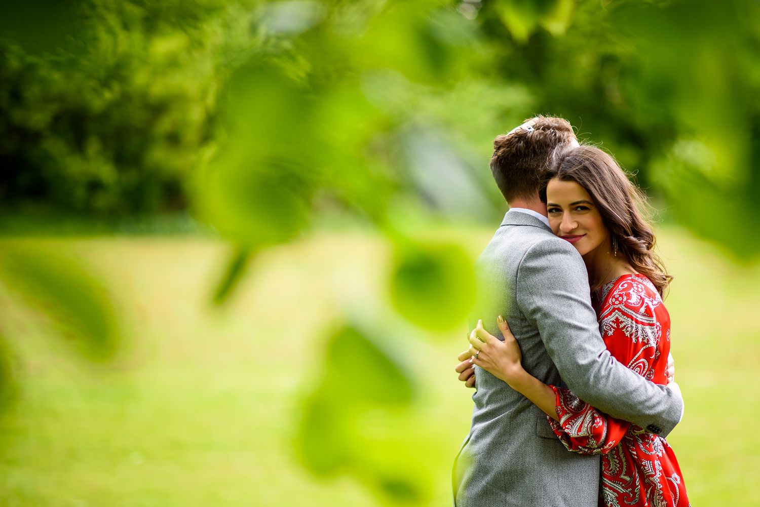 A romantic engagement photo with soft green foliage in the background.