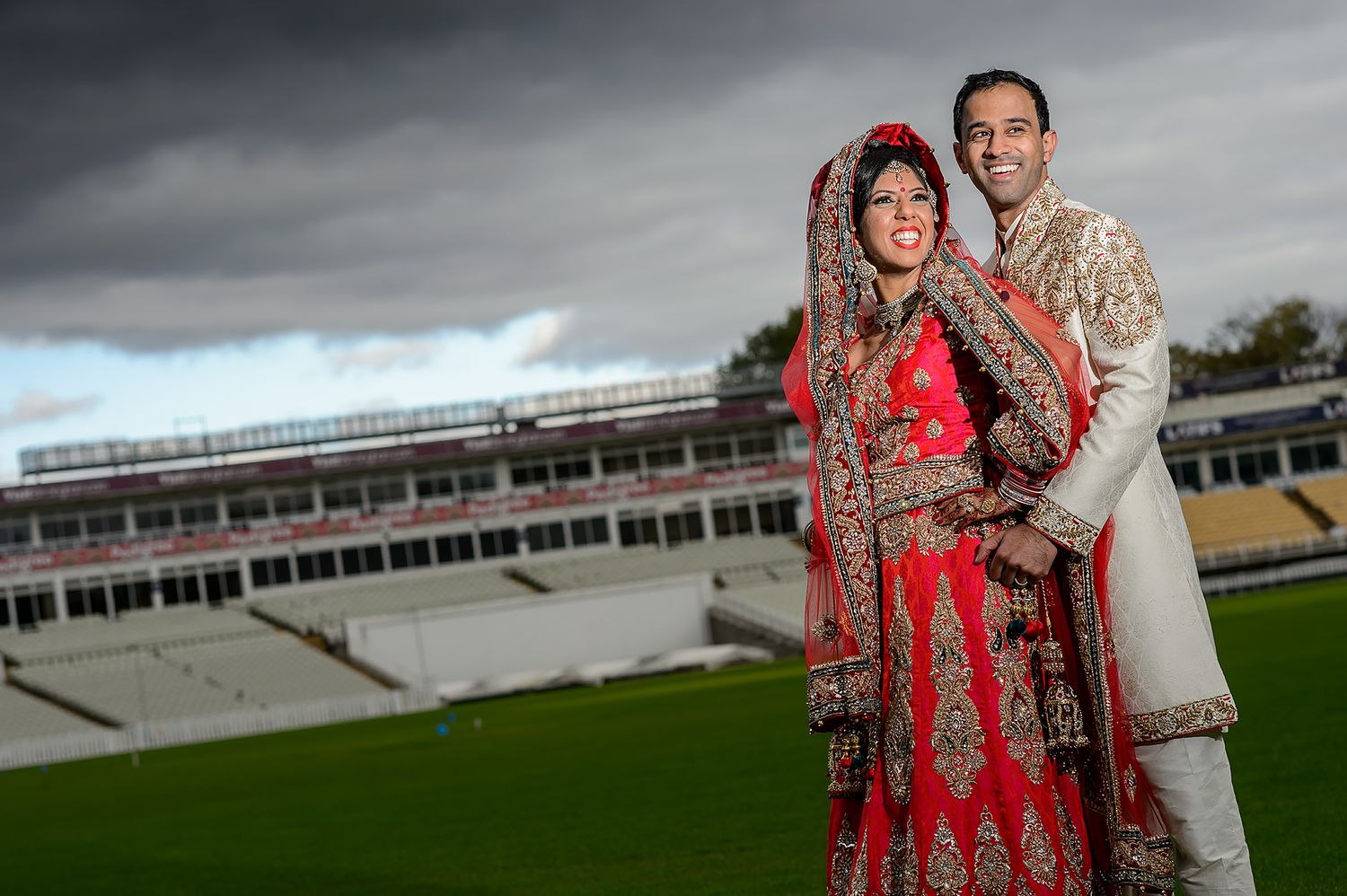 Wedding couple posing for portraits at a sports stadium under dramatic cloudy sky.