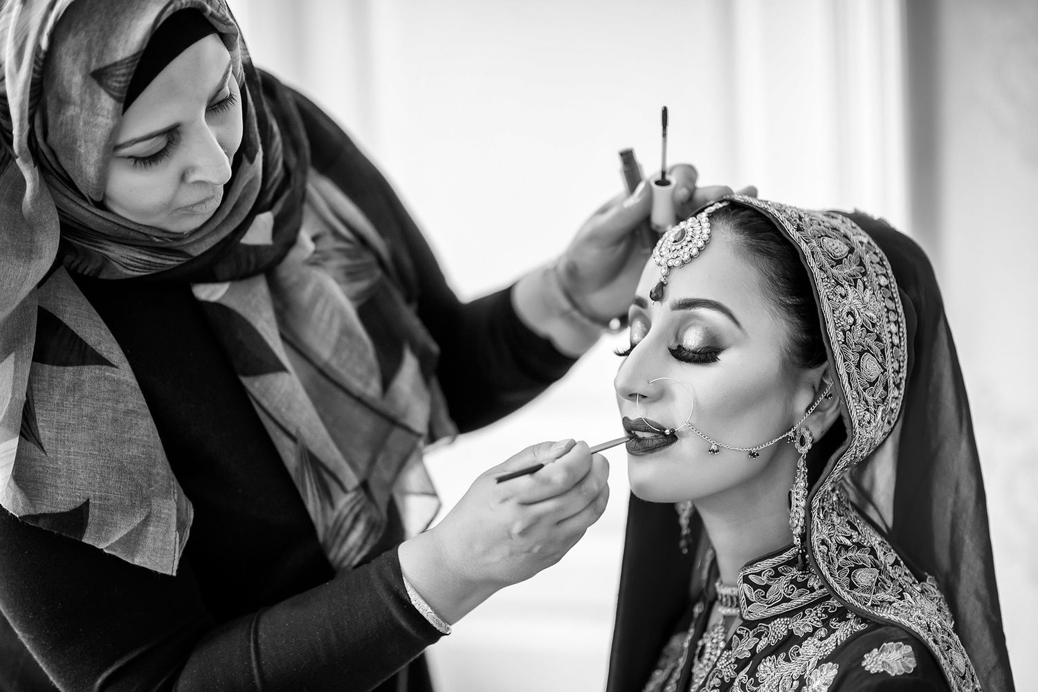Black and white photo of bridal makeup application in natural window light.