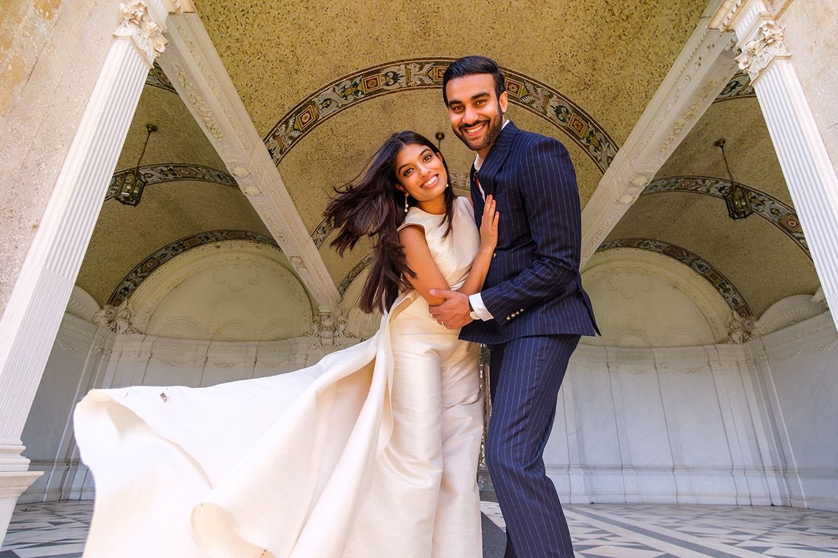 Happy couple dancing and twirling in an ornate white archway during their wedding celebration.