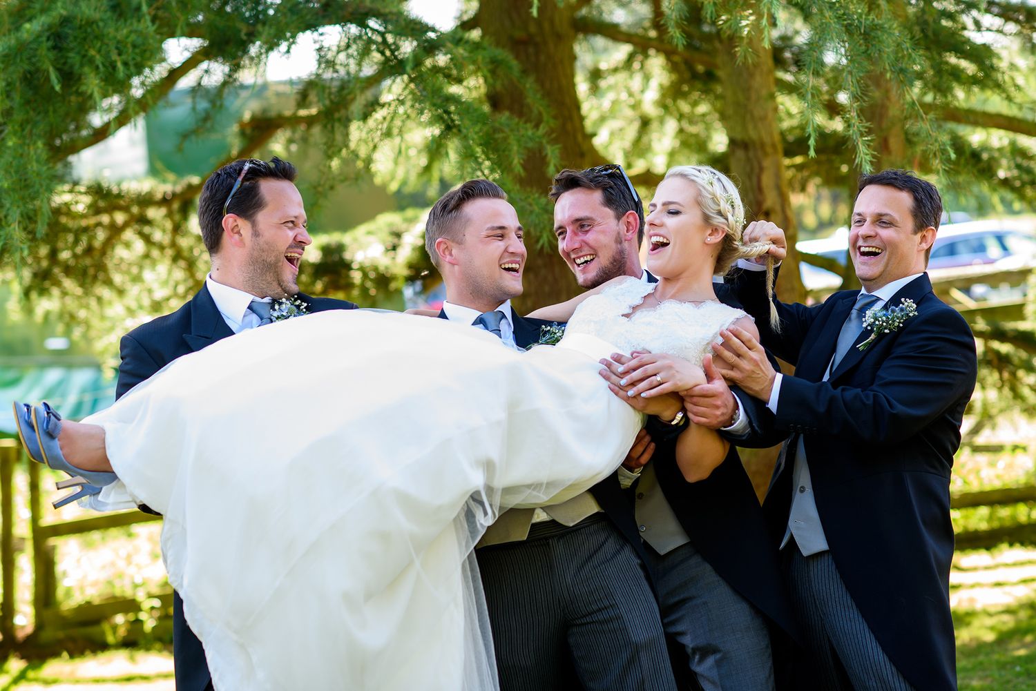 Wedding party having fun and celebrating with playful poses under green trees.