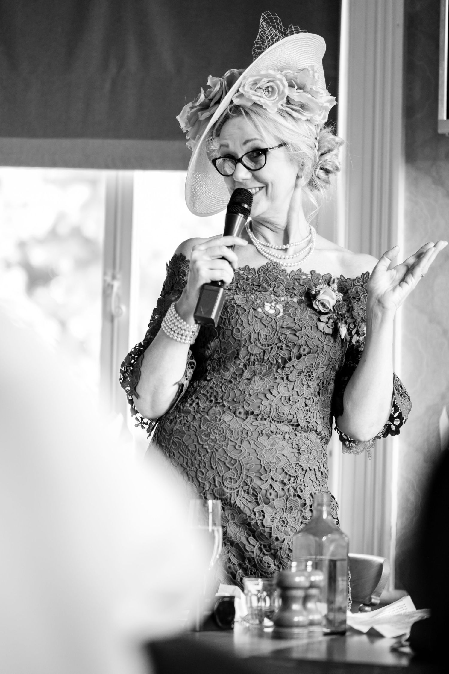 Performer in lace dress and ornate hat sings into microphone during vintage-style event.
