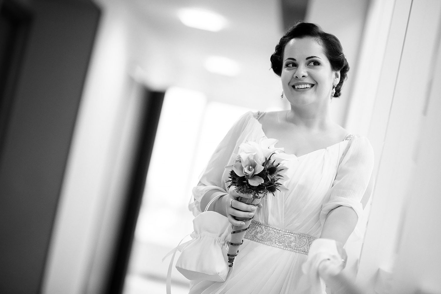 A joyful bride in a white wedding dress holding a bouquet in a hallway.