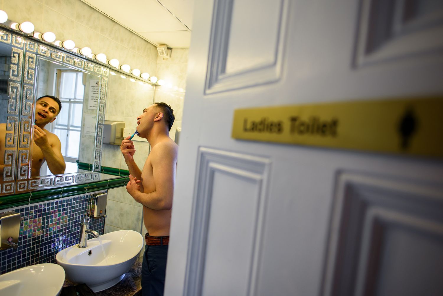 Interior view of a vintage-style bathroom with mirrored walls and Ladies Toilet sign.