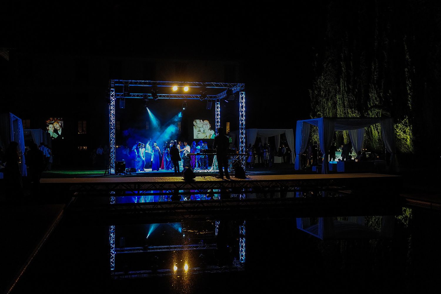 Concert stage illuminated with blue lights reflecting in water during nighttime performance.