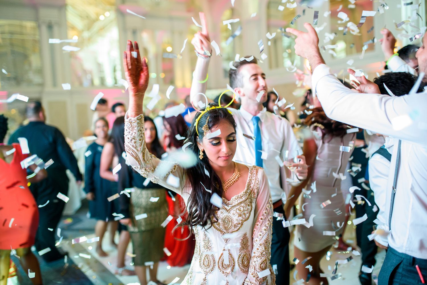 Wedding guests dancing joyfully and celebrating on a dance floor with confetti in the air.