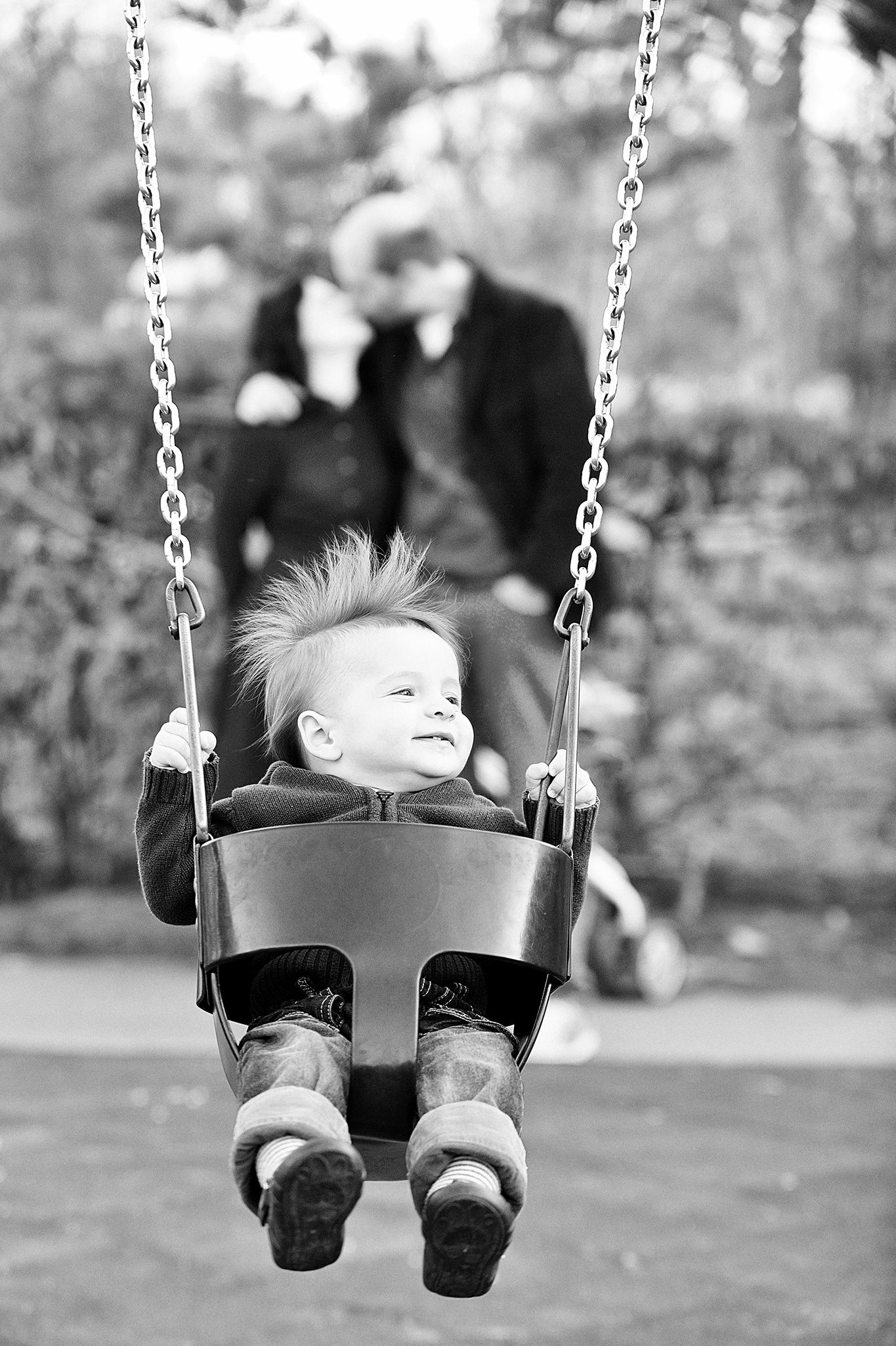 A small child enjoys a playful moment on a swing set while someone watches in the background.