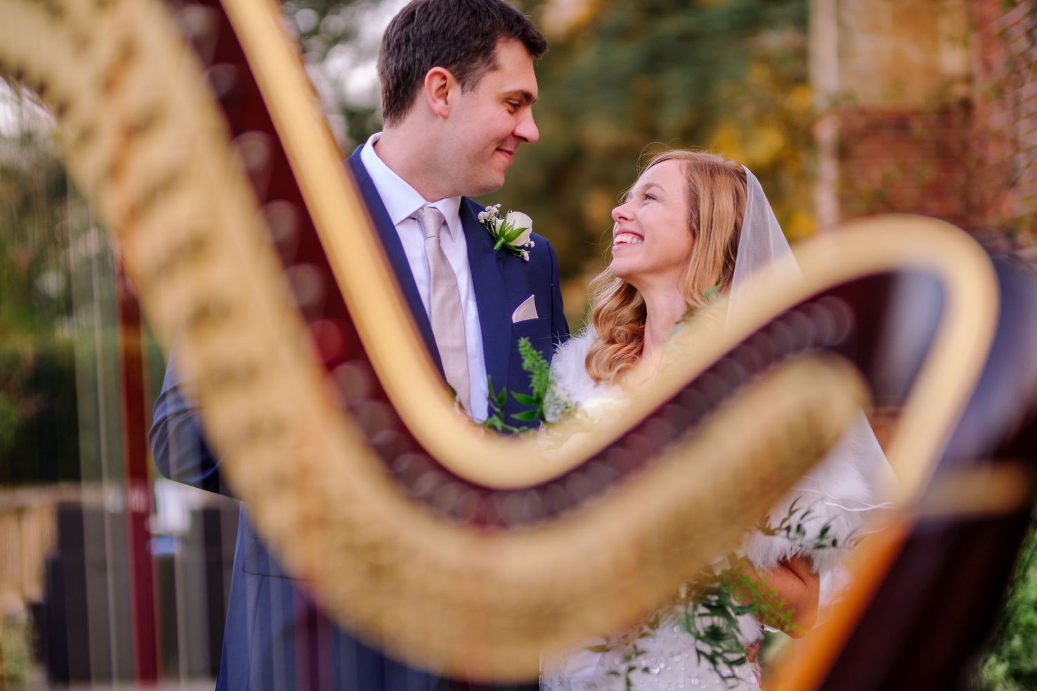 A romantic wedding moment captured through the curves of a golden harp during an outdoor ceremony.