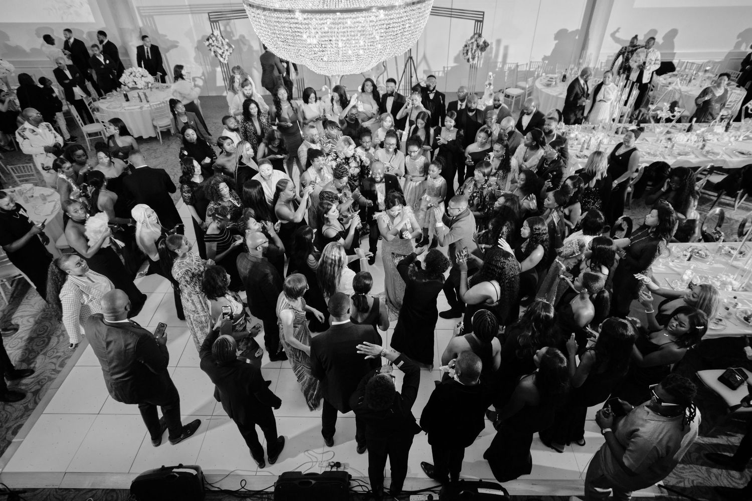 Large group of wedding guests dancing and celebrating on a crowded dance floor at an elegant reception venue.