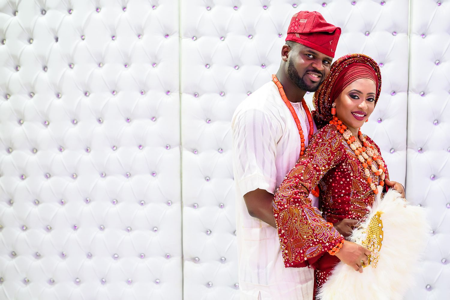 Couple in traditional red and gold attire dancing together against a white backdrop.
