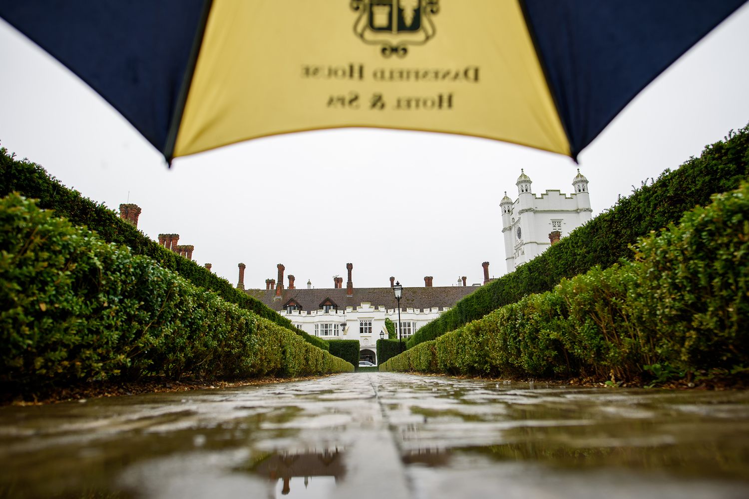 Dramatic wedding venue architecture shot through umbrella with wet cobblestones in foreground.