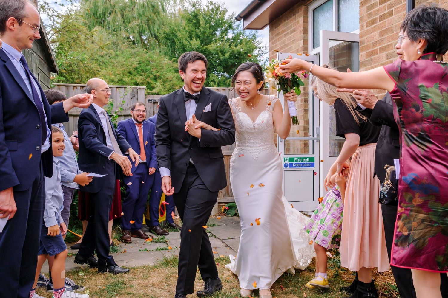 Wedding guests mingle and socialize outdoors during a garden reception on a sunny afternoon.