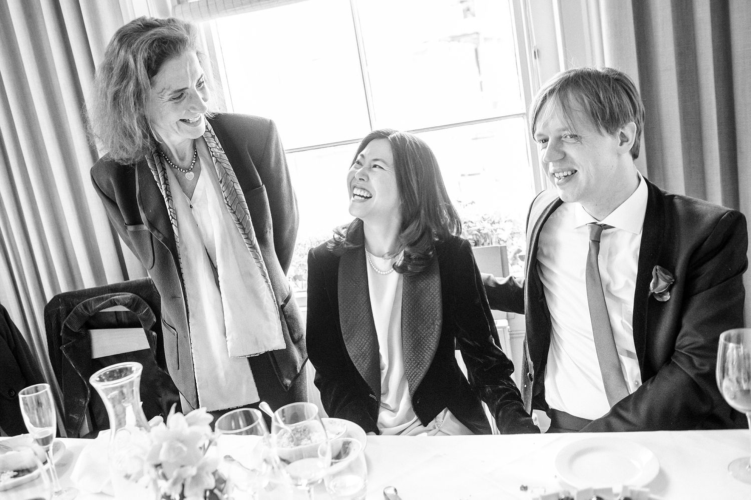 Candid black and white photo of guests sharing laughter at an elegant dinner party.