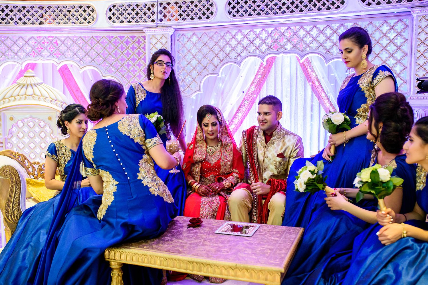 Wedding party members in blue attire gathered at decorated reception venue with purple accent lighting.