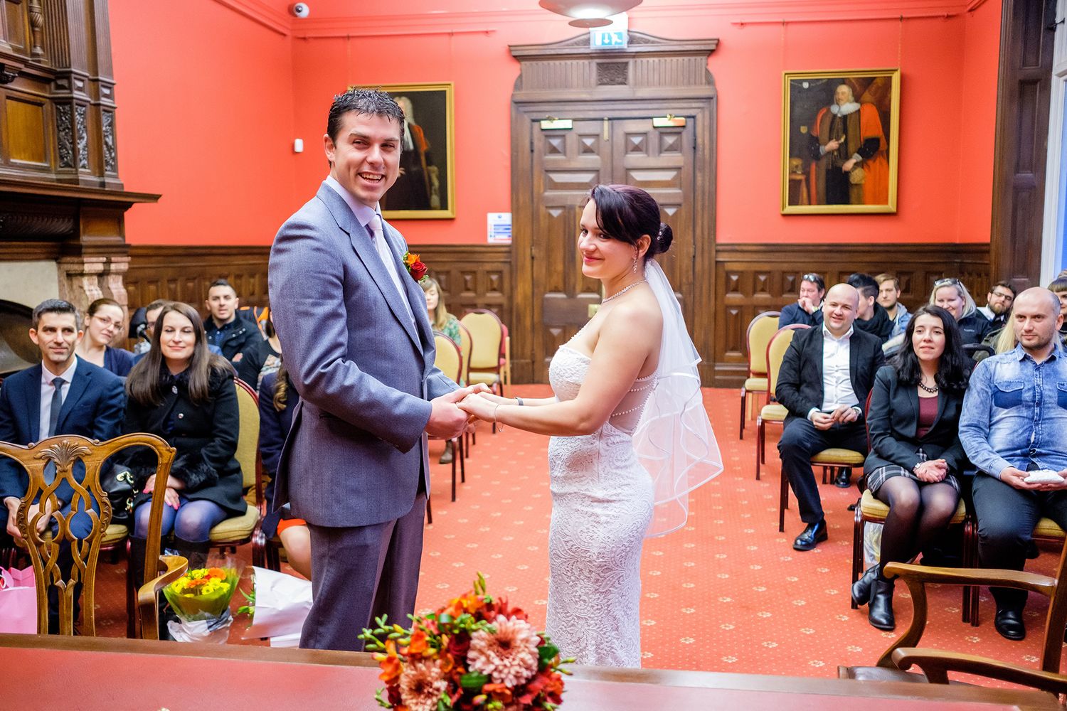 Wedding celebration in vibrant red-walled room with guests watching ceremony.