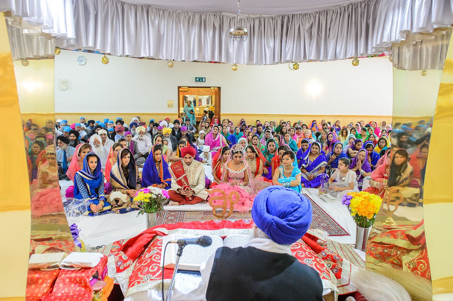 Large banquet hall decorated with white drapes and filled with guests at a celebration.