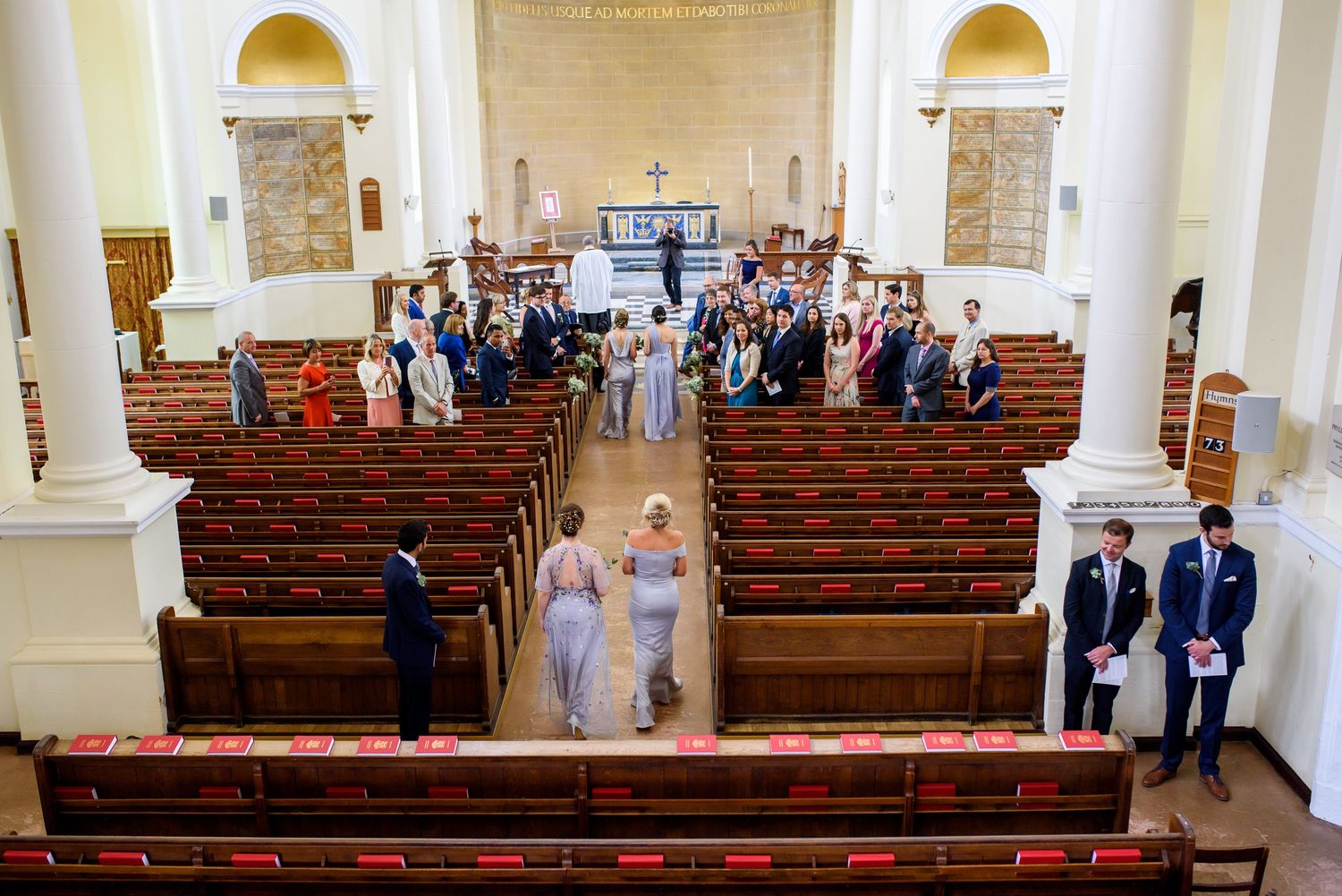 Interior view of traditional church sanctuary with wooden pews and white columns during wedding ceremony.