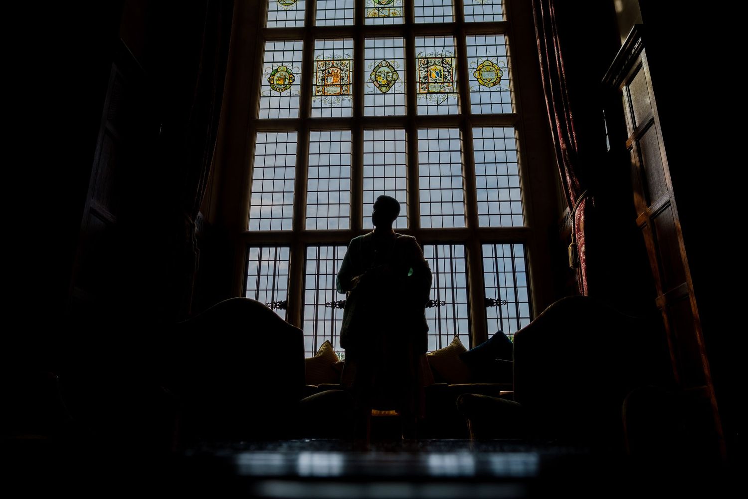Elegant interior of historic mansion with dark wood paneling and ornate windows casting dramatic shadows.