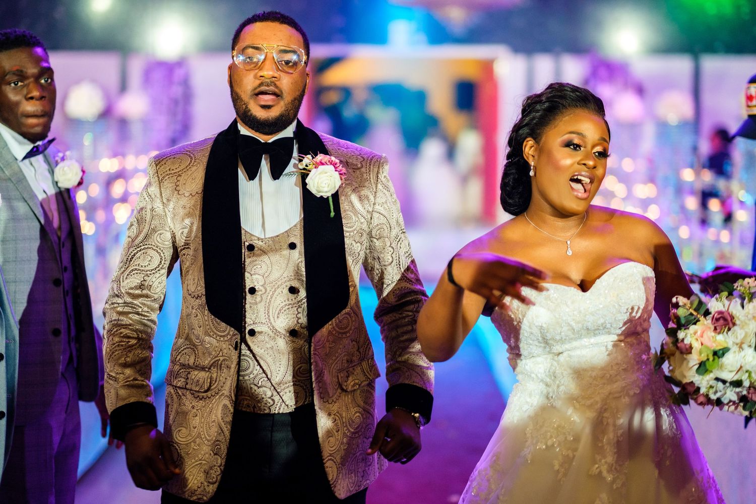 Wedding party members walking through reception venue with elegant lighting and decor.