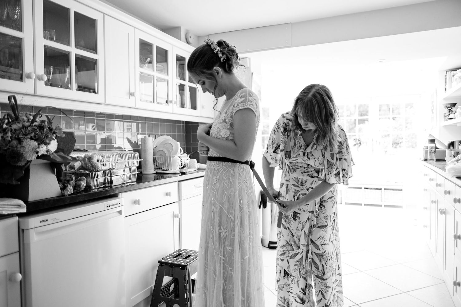 Candid black and white photo of wedding preparations in a bright kitchen setting.