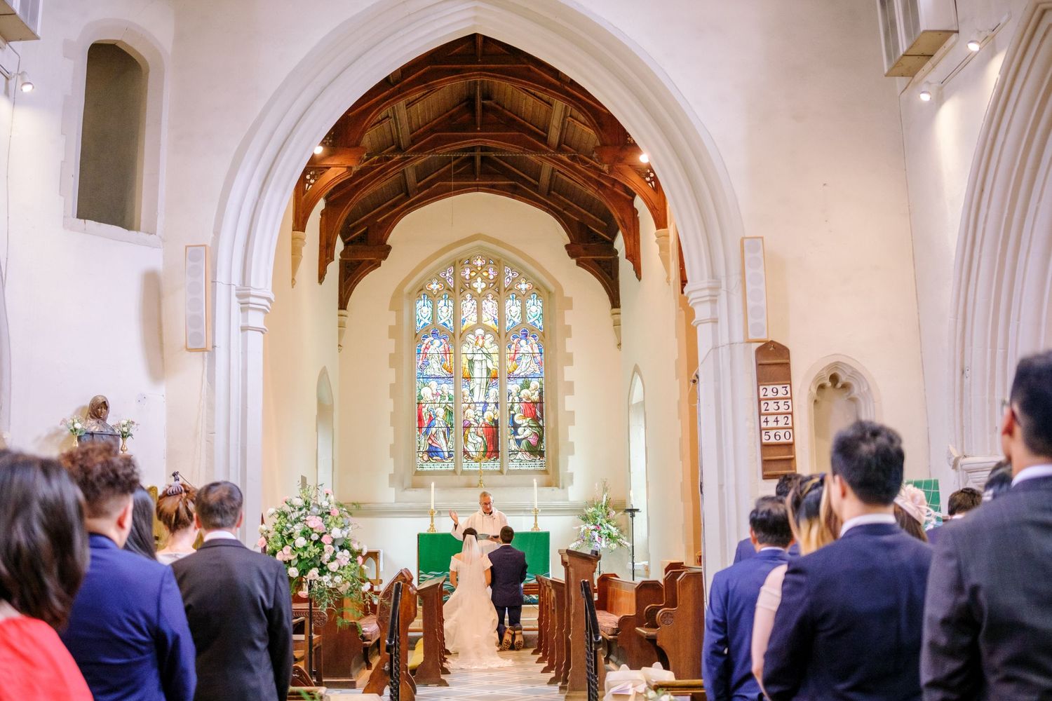 Church interior with white arched ceilings and stained glass windows during a wedding ceremony.