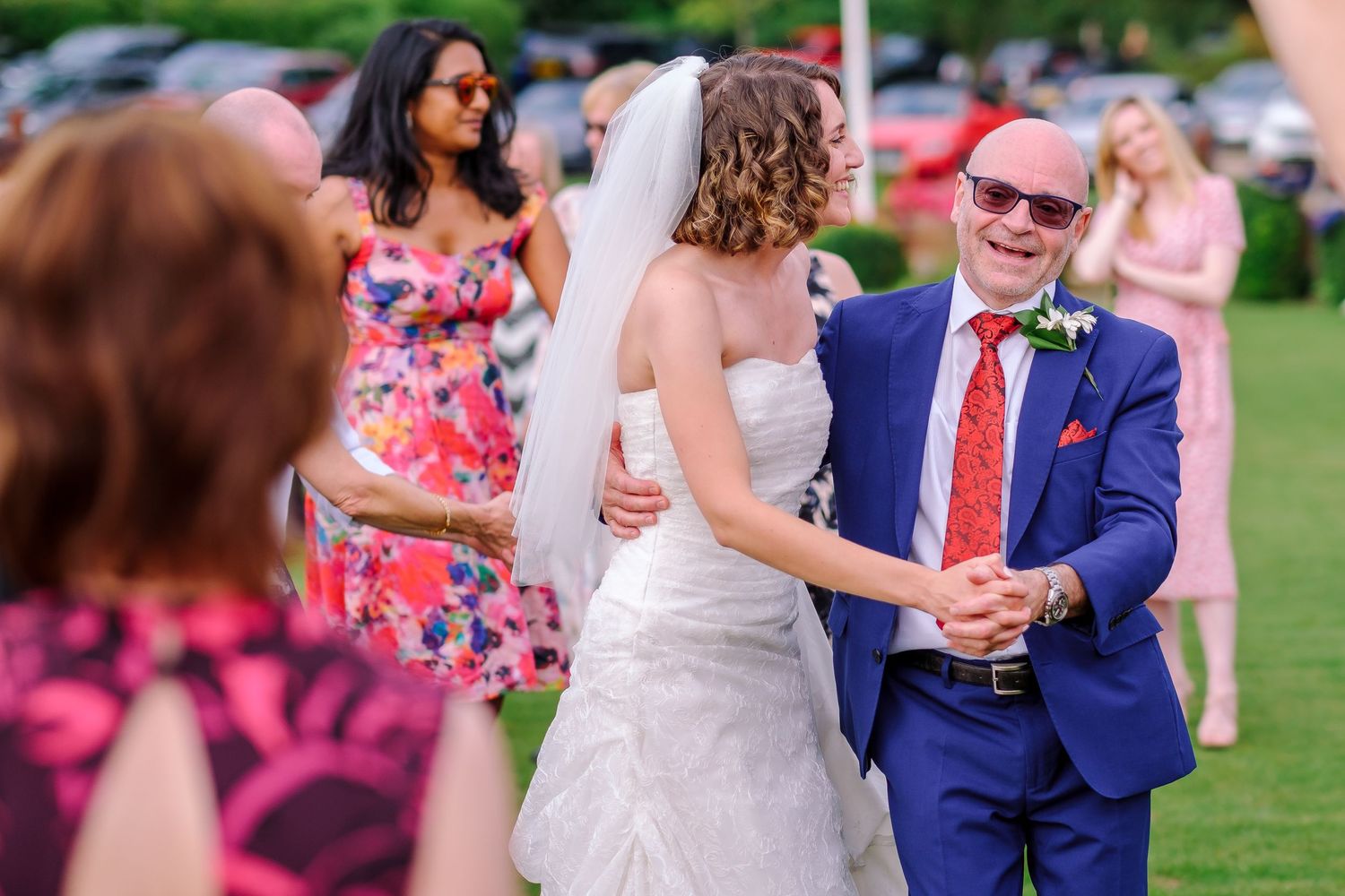Wedding party celebrates on a sunny lawn with guests in summer attire.