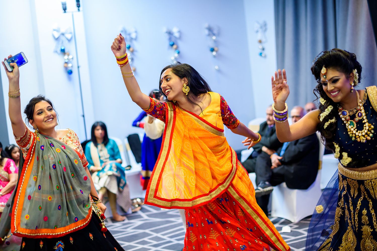 Colorfully dressed dancers perform traditional Indian dance moves at a festive celebration with vibrant orange and blue outfits.
