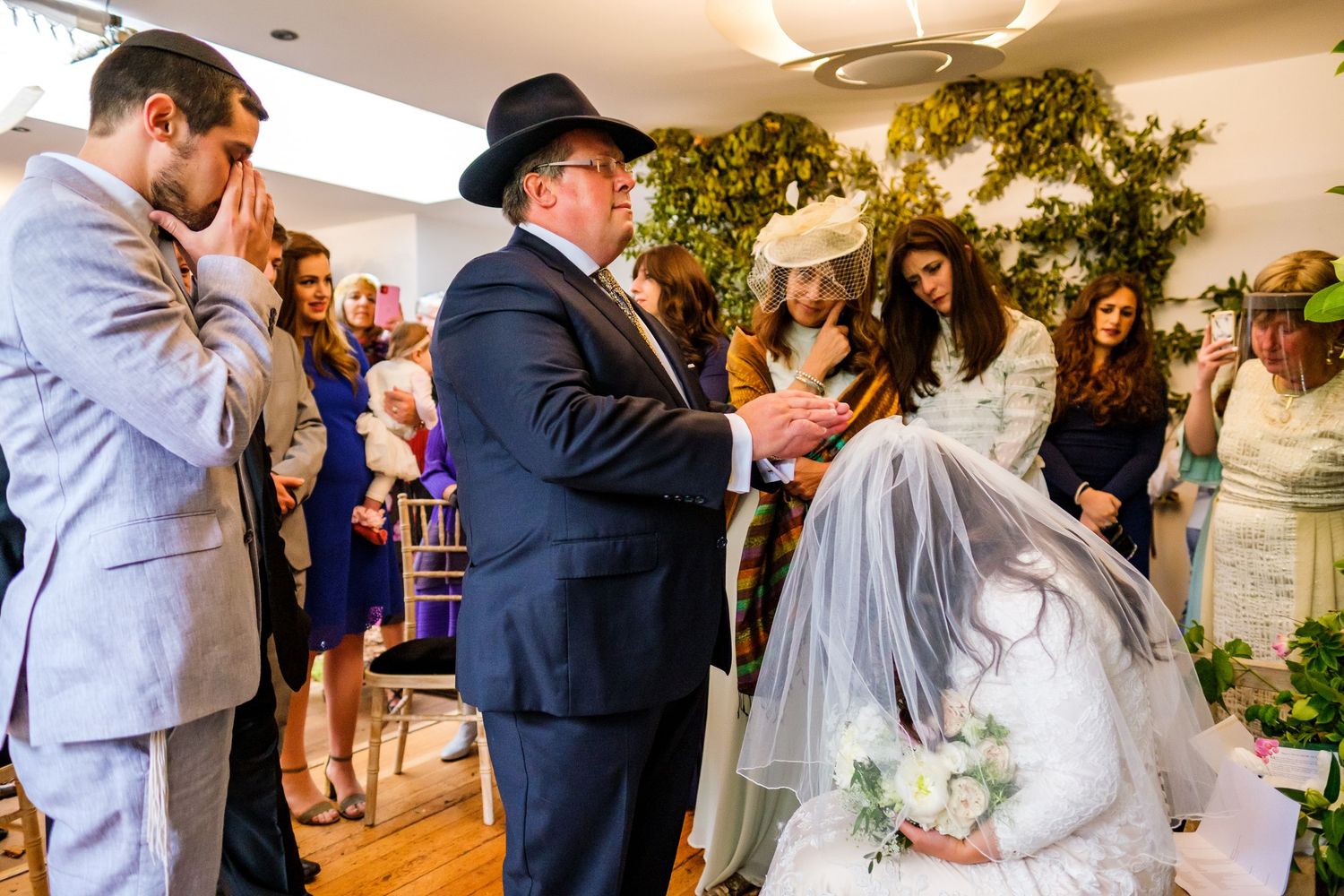 Wedding guests dancing and celebrating at an indoor reception venue decorated with greenery and lights.